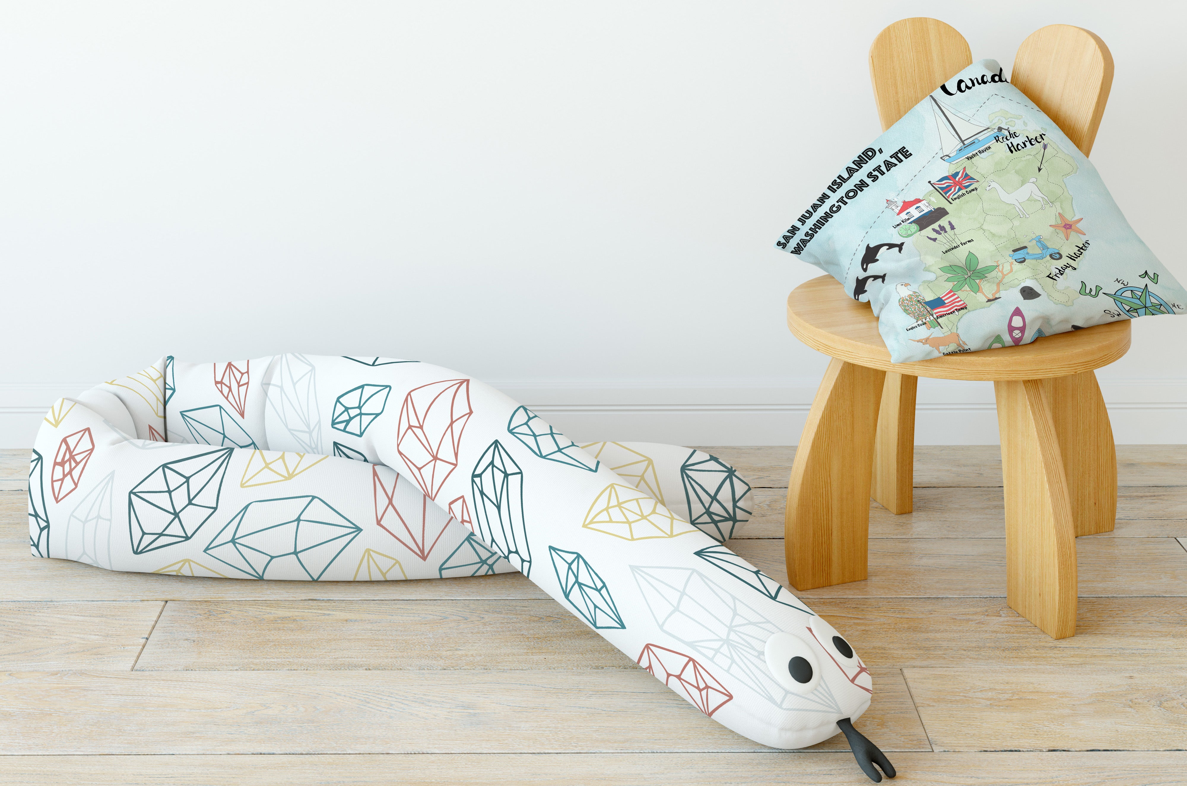 U-shaped children's body pillow with geometric pattern on a wooden floor, next to a small wooden stool with a decorative map pillow.